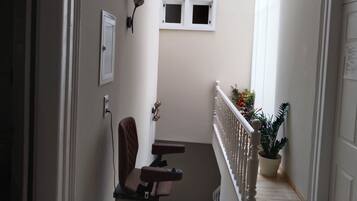 A narrow hallway with a chair, a small table, a potted plant, and a white door.