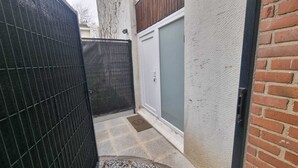 A narrow outdoor space with a metal gate, a white door, and a brick wall.