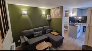 A modern living room with a sectional sofa, a small round table, and a kitchen area with a washing machine.