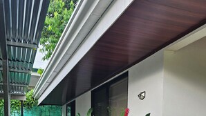 Un edificio con fachada blanca y tejado de madera. En frente, un jardín con plantas verdes y flores rojas.