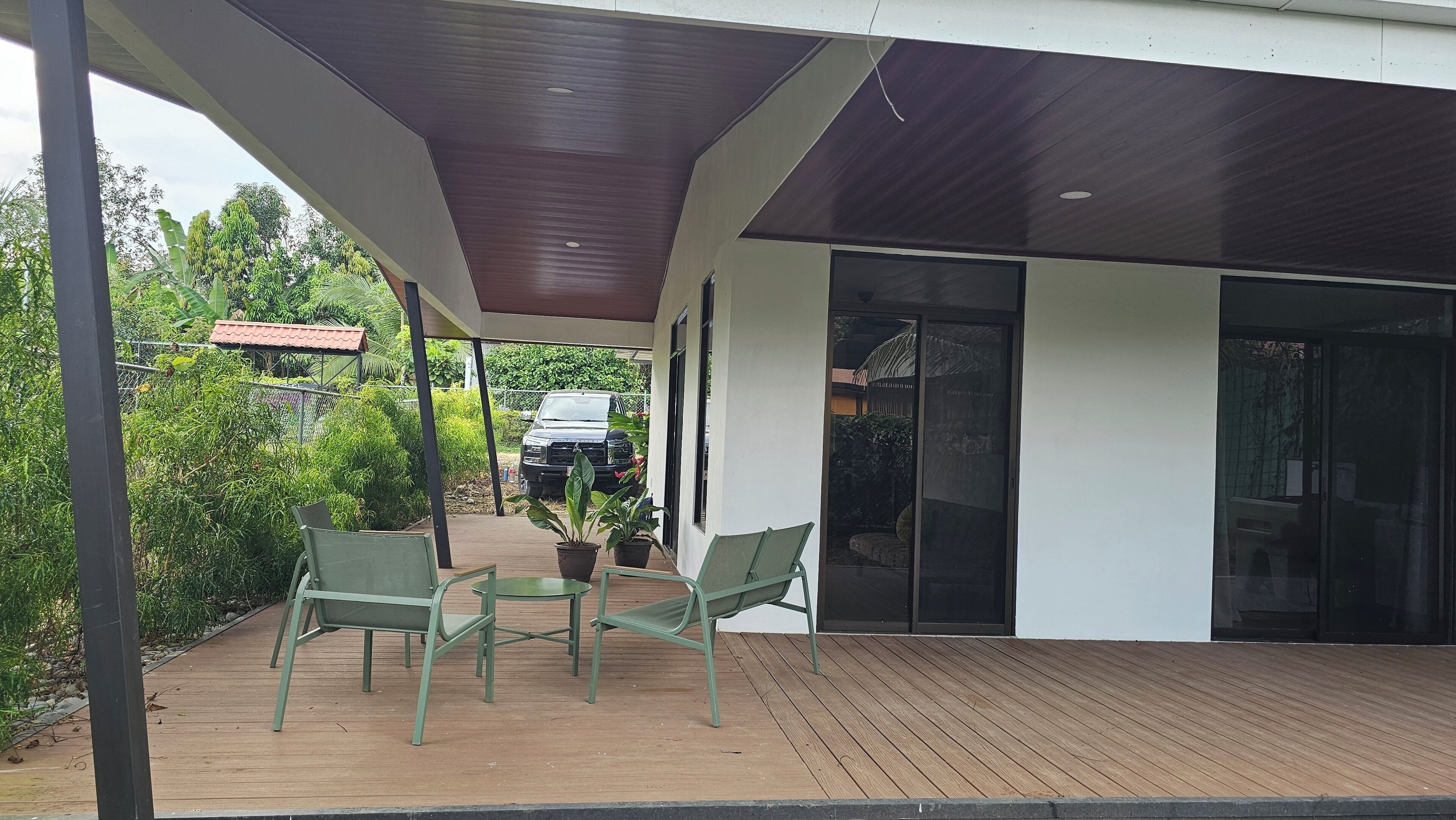 Un espace extérieur abrité doté d’une terrasse en bois, de deux chaises vertes et d’une plante en pot.