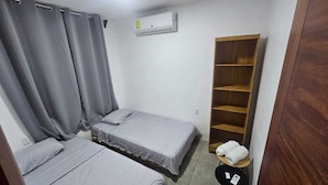 Una habitación pequeña y limpia con dos camas individuales, un armario de madera y un equipo de aire acondicionado en la pared.