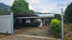 Un espacio exterior cubierto con un edificio blanco, rodeado de vegetación y un telón de fondo montañoso.