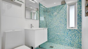 A modern bathroom with a white sink, a glass shower enclosure, and a tiled wall.