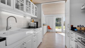 A modern kitchen with white cabinetry, a stainless steel sink, and an oven. There is a window with a view of the outdoors.