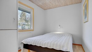 A small, single-bed room with a window, a radiator, and a wall-mounted lamp.