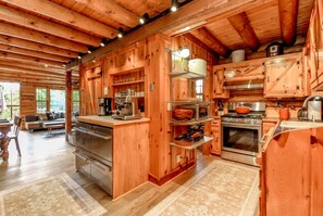 A wooden cabin interior with a kitchen featuring stainless steel appliances, wooden cabinets, and a dining area with a sofa and table. - 5 Miles to Rainier`s Nisqually Entrance – 8 Private Acres + Hot Tub (Ashford)