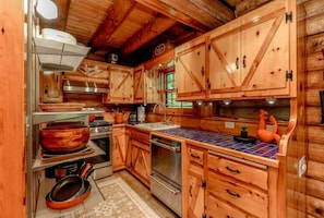 Interior de una cabaña de madera con cocina, que incluye armarios de madera, una estufa y un lavabo.