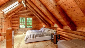 Ein Schlafzimmer in einer Blockhütte mit einem Bett, einem Nachttisch und einem Fenster.