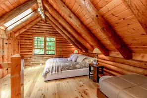 Une chambre à coucher située dans une cabane en rondins, avec un lit, une table de chevet et une fenêtre.