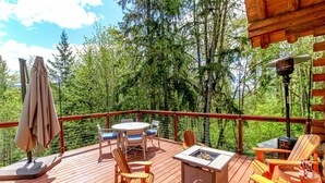 A wooden deck with outdoor furniture, including chairs and a table, surrounded by trees.