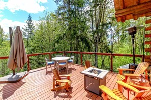 A wooden deck with outdoor furniture, including chairs and a table, surrounded by trees.