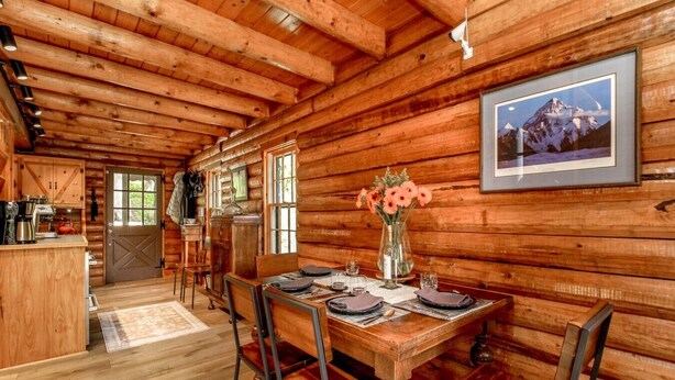 Ein Holzblockhaus-Interieur mit Esstisch für vier Personen, einer Küchenzeile und einem gerahmten Bild an der Wand.