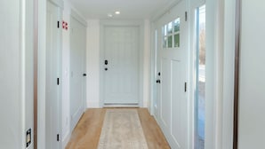 Corredor com portas brancas, um tapete bege e vista para uma paisagem nevada através de uma porta de vidro.