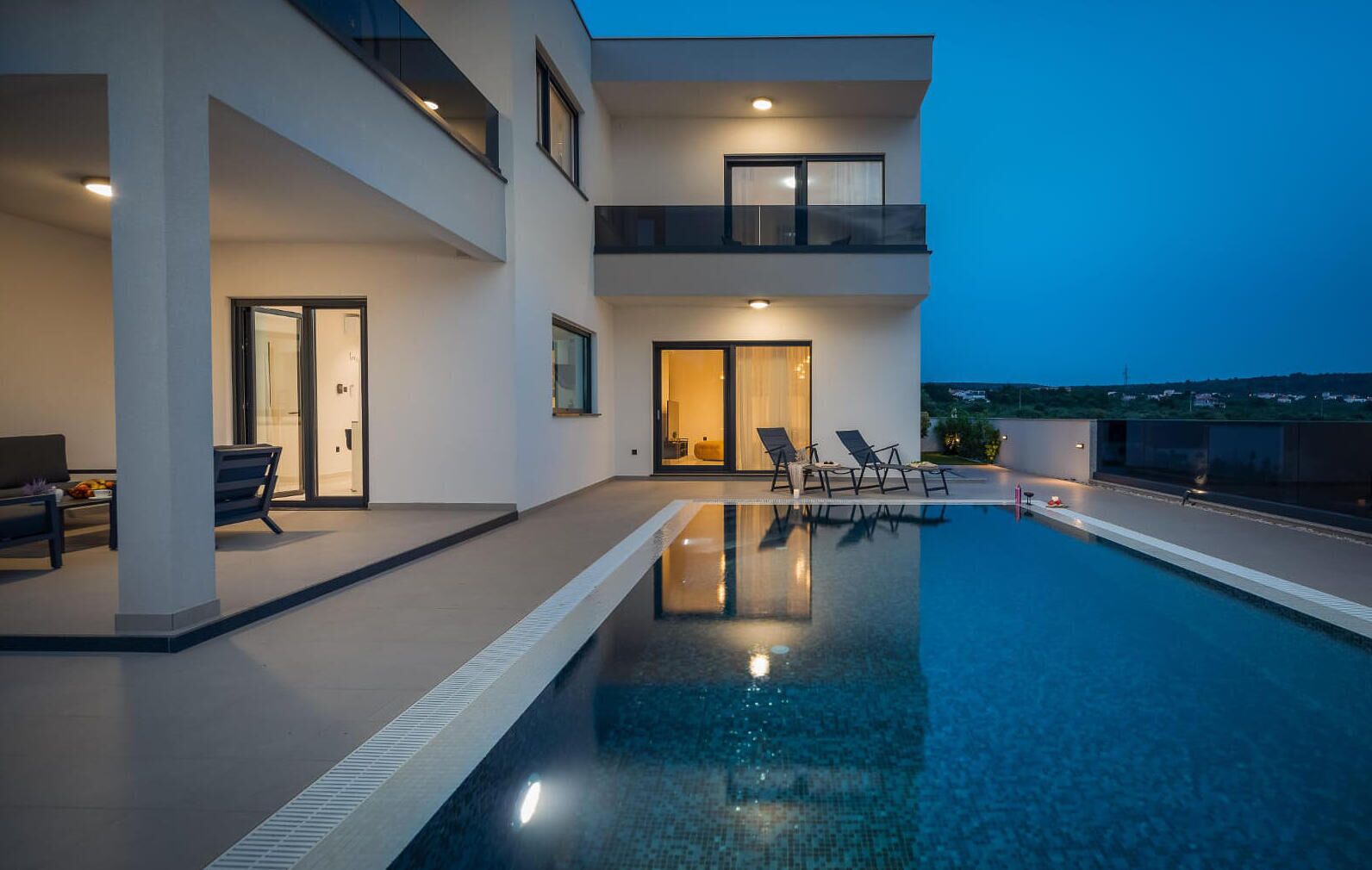 Um edifício moderno de dois andares com piscina, área de estar externa e vista para a paisagem.
