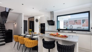 A modern kitchen with a central island, dining area with yellow chairs, and a large window overlooking a building. - Awesome home in Primosten (Primosten)