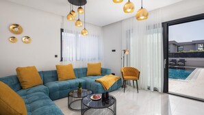 A modern living room with a teal sofa, mustard cushions, a round coffee table, and a view of a swimming pool through a glass door. - Awesome home in Primosten (Primosten)