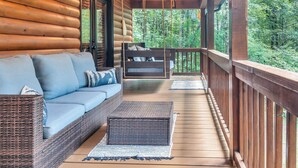 Una cabaña de troncos con una terraza de madera, un sofá con cojines y un columpio.