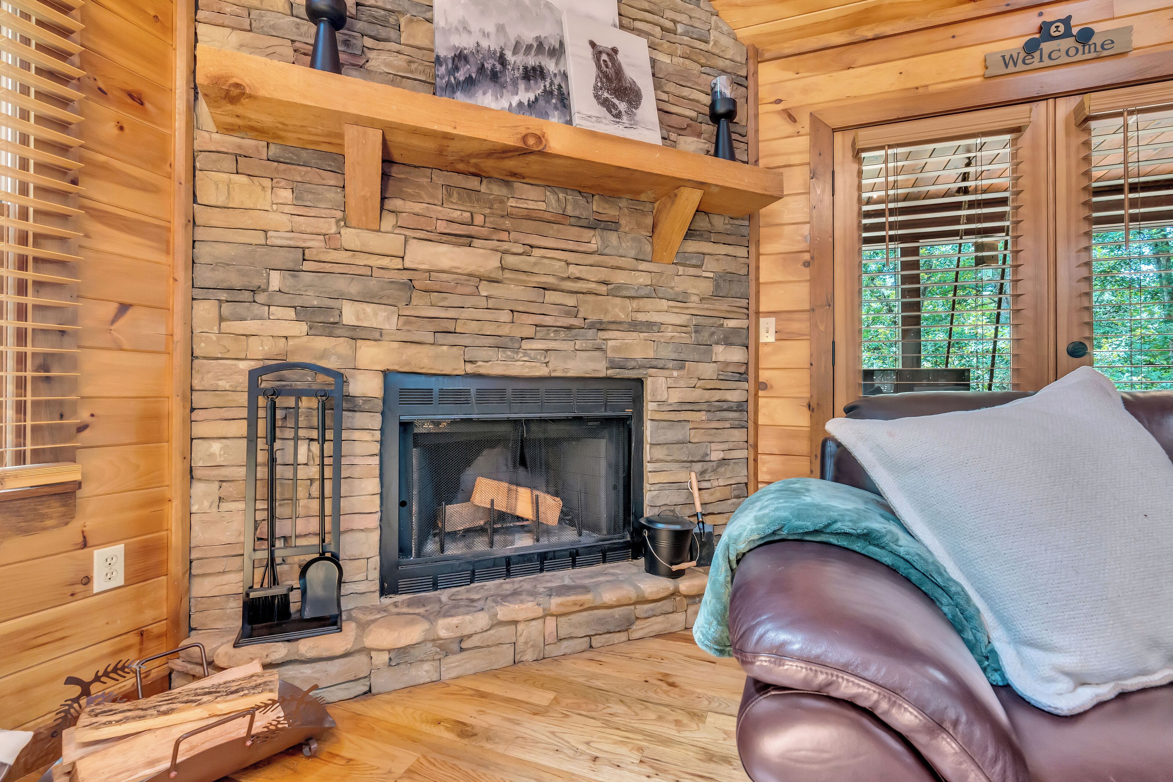 A cozy cabin interior with a stone fireplace, wooden walls, and a leather couch.
