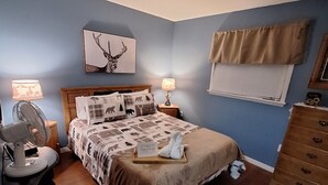 A bedroom with a bed, two bedside tables, a dresser, a ceiling fan, a wall-mounted lamp, and a framed picture. - Private cabin in Boisdale. Perfect getaway for the whole family with a view! (Boisdale)