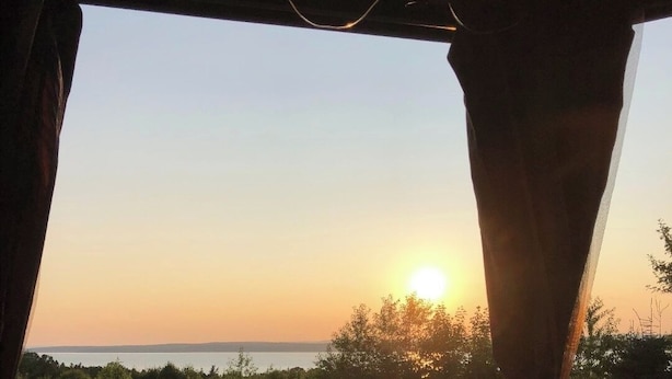 A wooden deck with a view of the sunset over a body of water, surrounded by trees.