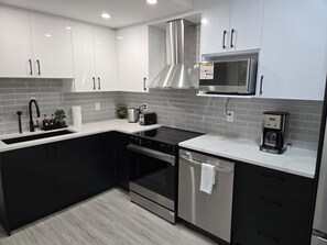 A modern kitchen with a stainless steel range hood, a microwave, and a coffee maker. - Family Friendly Home away from Home! (Calgary)