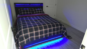 A bed with a plaid bedspread and blue LED lighting underneath.