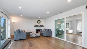 Un salon moderne avec une cheminée, deux canapés gris et un pouf à motifs.