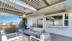 Une terrasse extérieure couverte, dotée d’un espace salon, d’un foyer et d’une pergola agrémentée d’un luminaire suspendu.