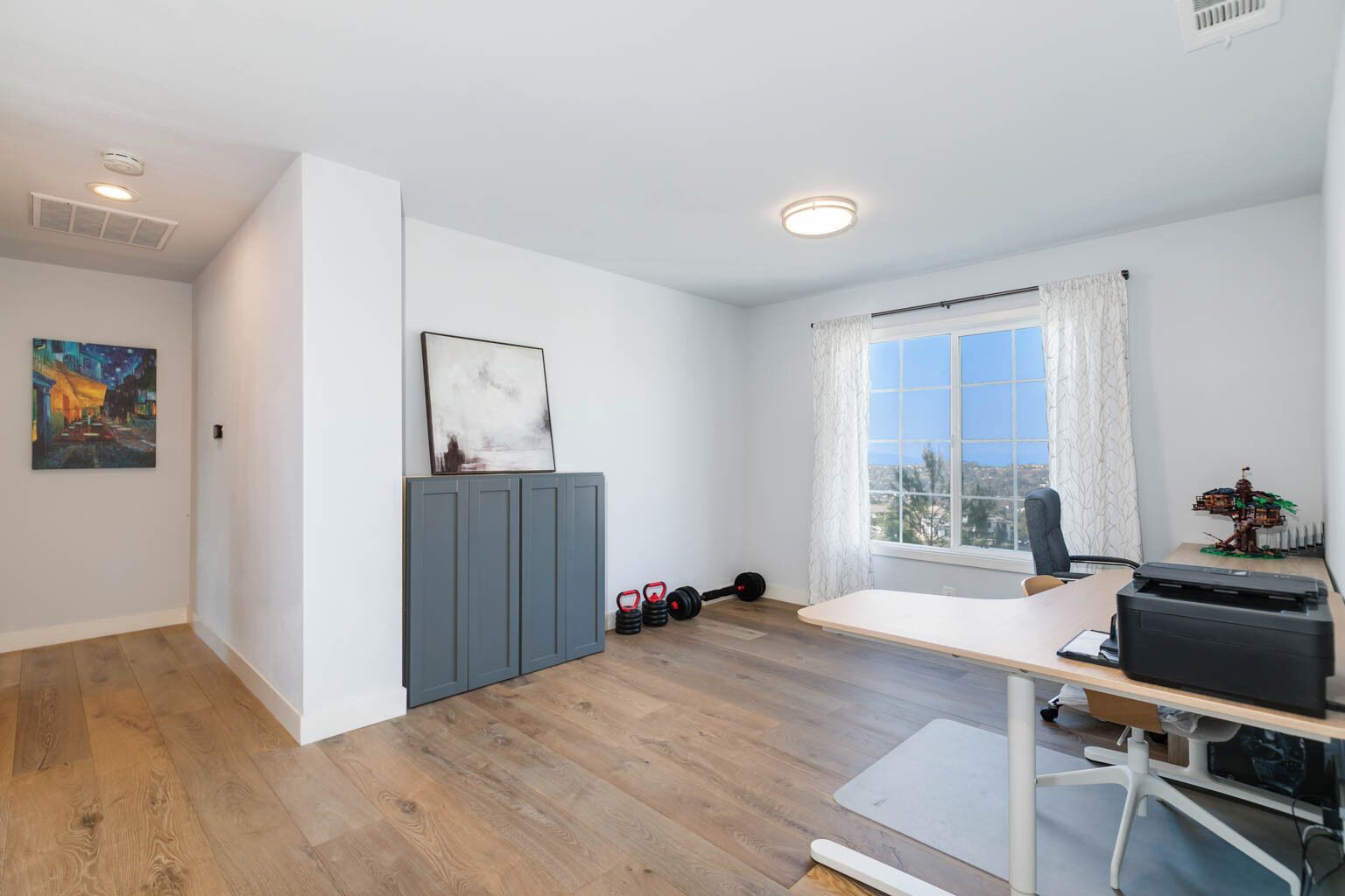Una habitación moderna con escritorio, silla y vistas de la ciudad a través de un ventanal grande.