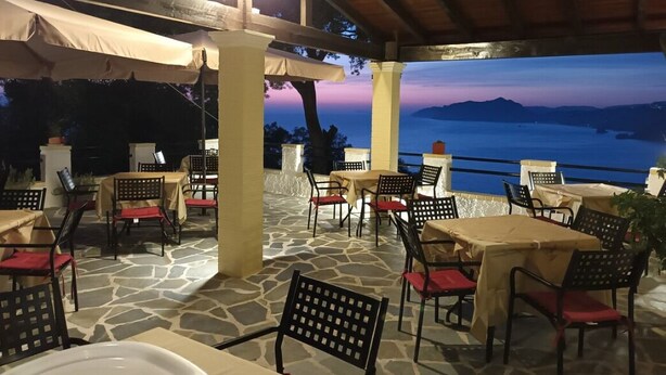 An outdoor patio with stone flooring, tables, and chairs, overlooking a body of water and hills at dusk. - Charming 2-bedroom house with AC, WiFi in amazing Corfu






 (Corfu)