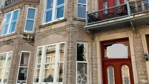 A multi-story building with a red door, multiple windows, and a balcony with a metal railing. - Vieux Quebec- au cœur - Old Quebec (Québec)