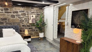 A bedroom with a stone wall, a bed with white bedding, a bedside table with a lamp, and a wooden cabinet. - Vieux Quebec- au cœur - Old Quebec (Québec)