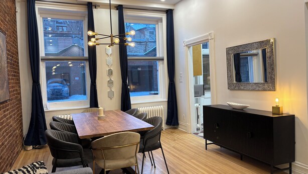 A dining area with a wooden table, black chairs, a chandelier, and a black cabinet with a mirror. - Vieux Quebec- au cœur - Old Quebec (Québec)