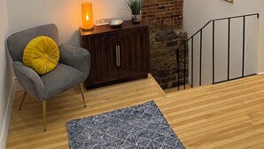 A modern living room with a grey armchair, a yellow cushion, a wooden cabinet, a black and white rug, and a brick wall accent. - Vieux Quebec- au cœur - Old Quebec (Québec)