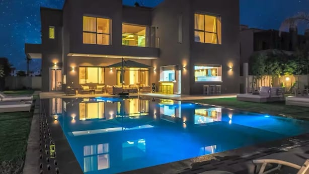 Ein modernes, zweistöckiges Haus mit Swimmingpool, Außenbeleuchtung und einem gepflegten Rasen.