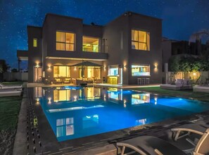A modern two-story house with a swimming pool, outdoor lighting, and a well-maintained lawn.