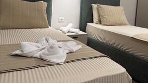 Hotellihuoneessa on kaksi sänkyä, joissa on molemmissa raidallinen vuodevaatteisto ja tyynyt. Sänkyjen välissä on yöpöytä, jossa on lamppu.