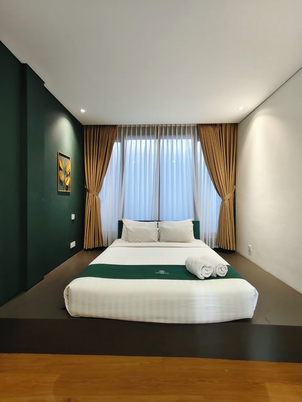 Een hotelkamer met een groot bed, gordijnen en een schilderij aan de muur.