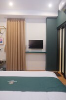 Quarto de hotel com cama, televisão presa na parede, janela com cortinas e porta para uma varanda.
