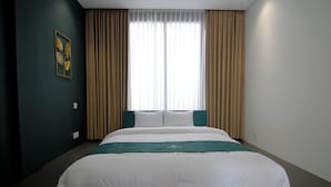 Hotellihuone, jossa on suuri sänky, beigenväriset verhot ja seinällä oleva kehystetty taideteos.