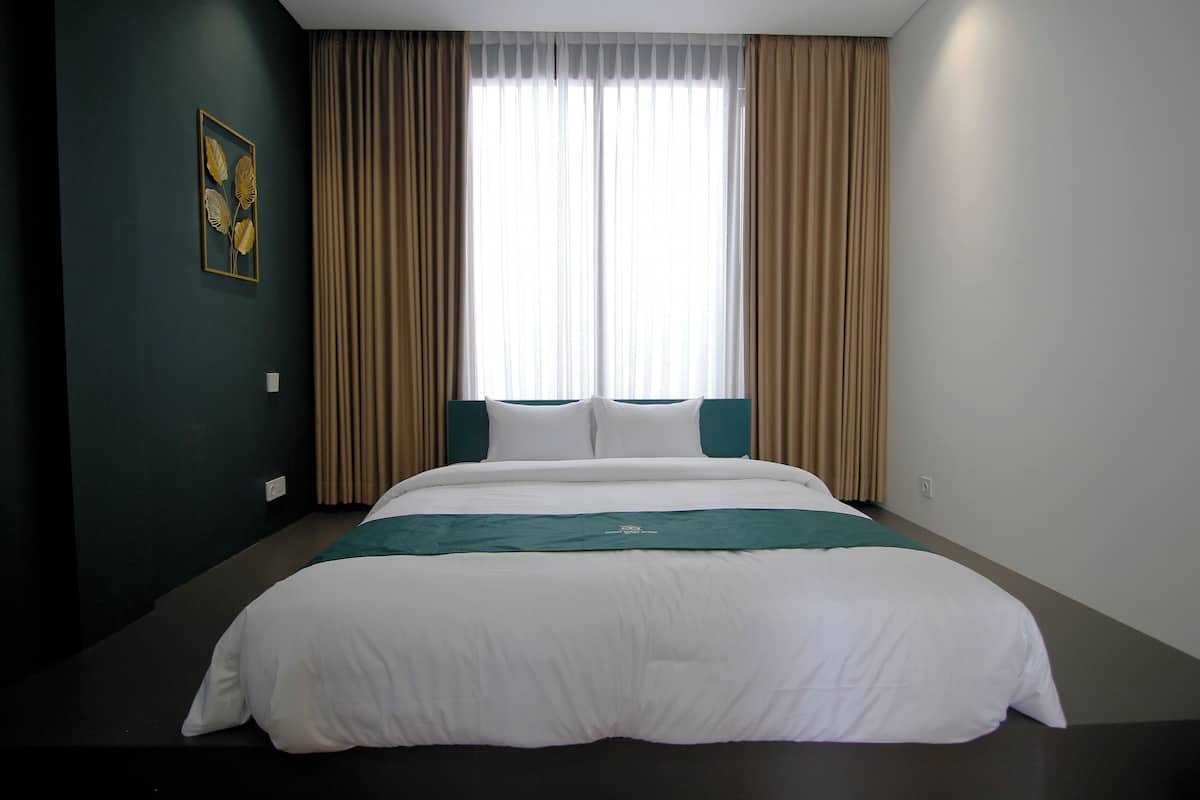 Ein Hotelzimmer mit einem großen Bett, beigefarbenen Vorhängen und einem gerahmten Kunstwerk an der Wand.