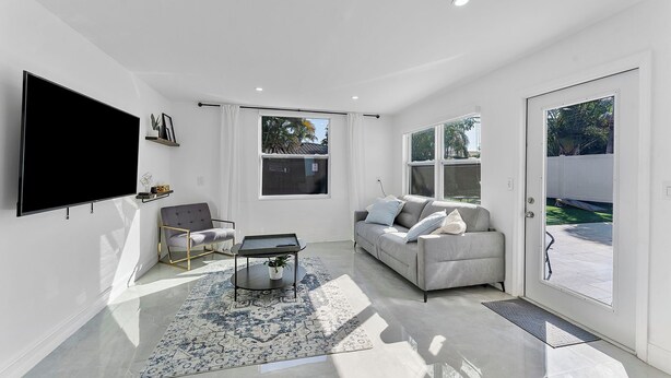 A modern living room with a flat-screen TV, a grey sofa, a coffee table, and a patterned rug.