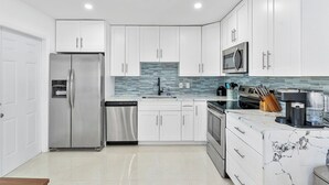 A modern kitchen with white cabinets, stainless steel appliances, and a marble countertop.