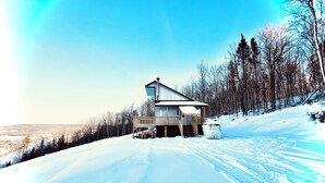 Eine Holzhütte mit Veranda, umgeben von verschneitem Gelände und Bäumen.