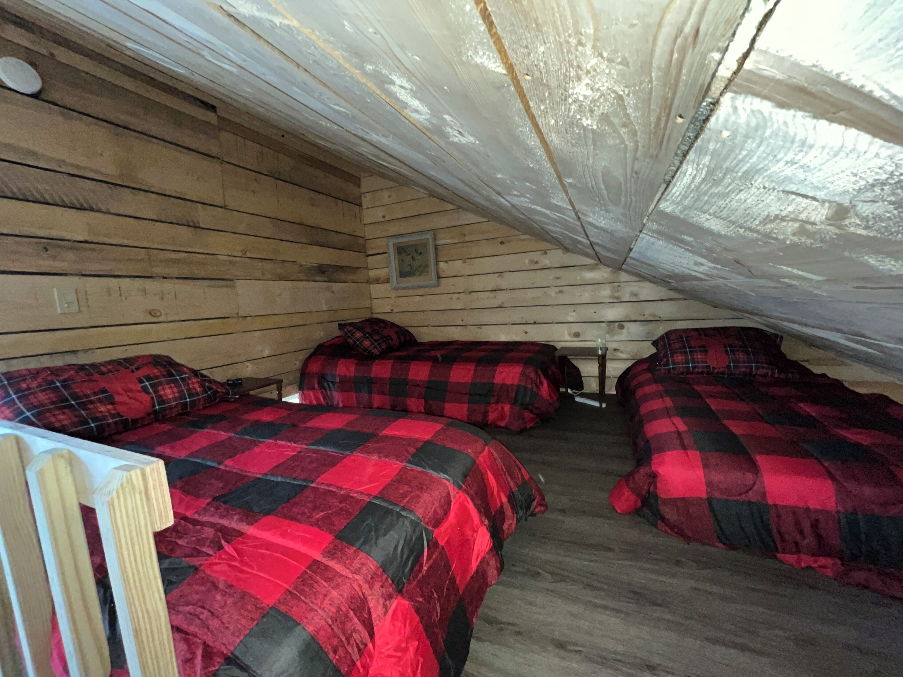Een blokhut met twee bedden, elk voorzien van rood-zwart geruit beddengoed, houten wanden en een schuine kap.