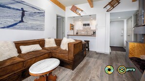 A modern living room with a brown leather sofa, a marble coffee table, and a ski-themed painting on the wall. - Lavender Lodge (#237) On ski slope | Triple-decker bunk beds! (Basye)