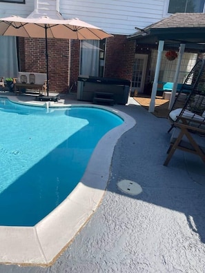 A swimming pool with a patio area, a covered seating area, and a brick wall. - Your Charming Getaway w/ Game Room & Pool Oasis (Houston)
