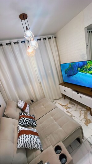 Een moderne woonkamer met een beige bank, een televisie op een houten dressoir en een geometrische lamp.