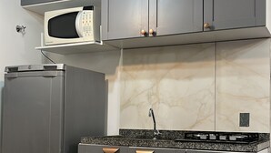 Cozinha moderna com armários cinza, micro-ondas, geladeira e painel de fundo em mármore.